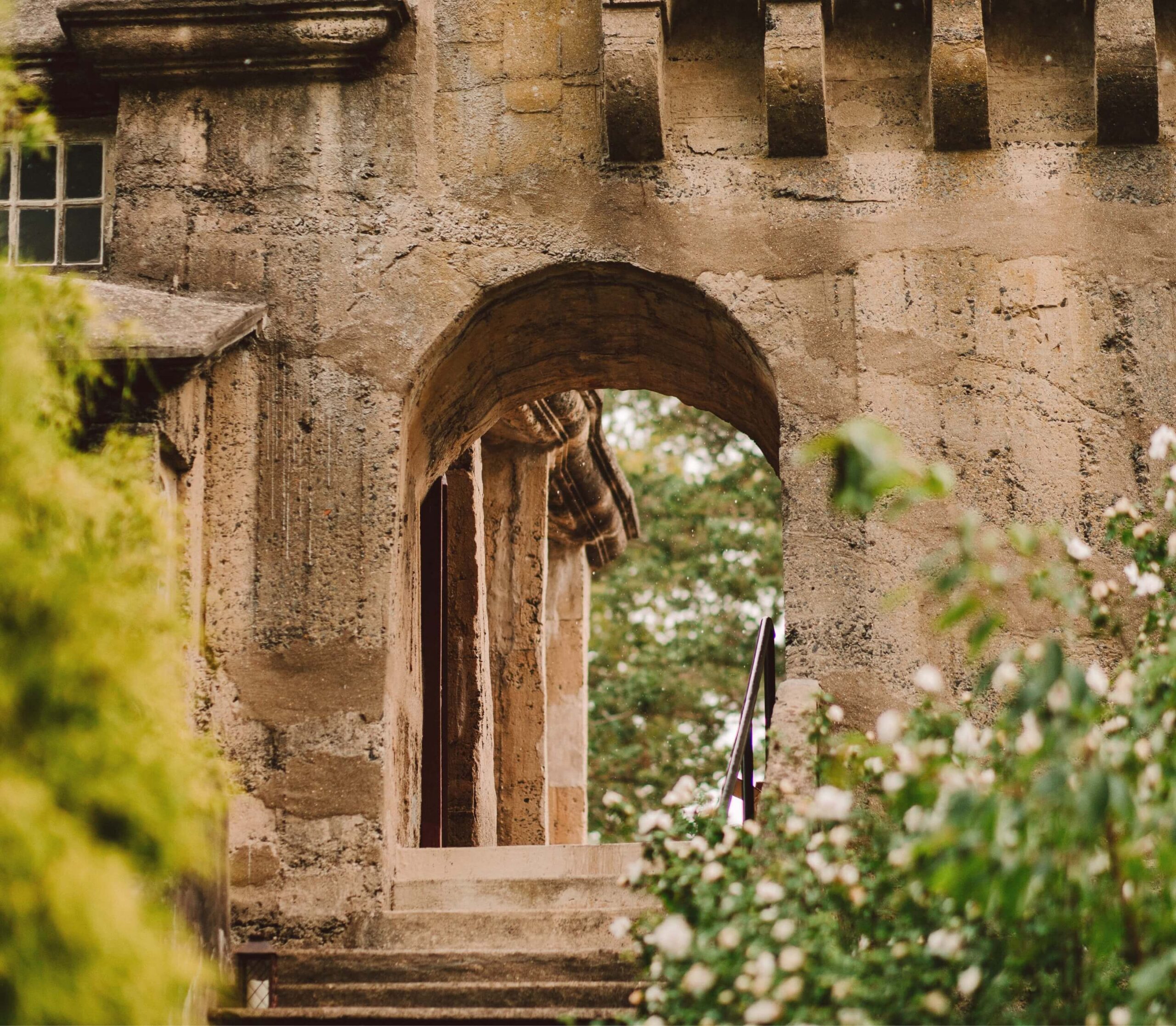 Stone archway with steps, surrounded by greenery, leading to an open entrance.