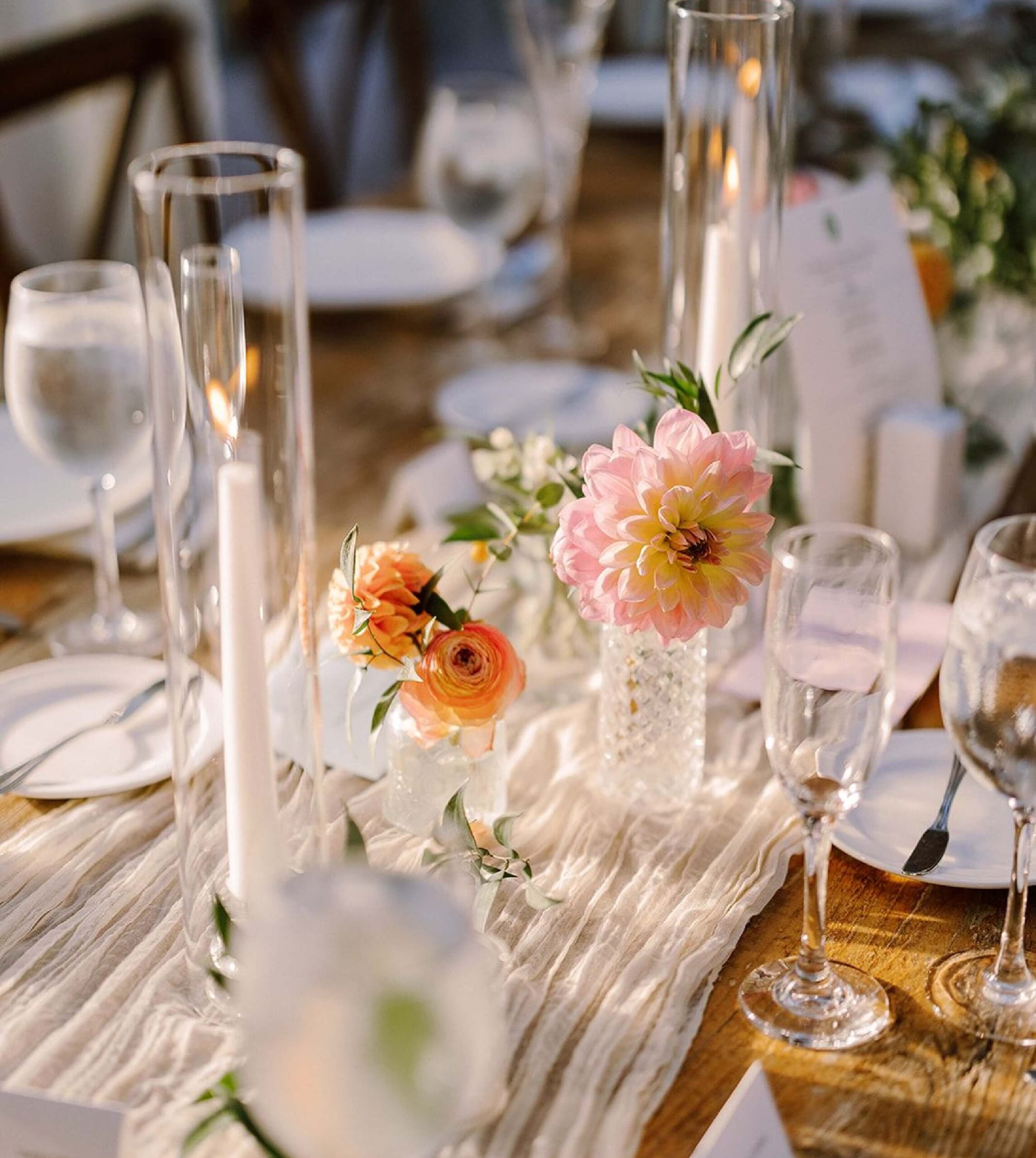 Elegant table setting with flowers, candles, wine glasses, and water goblets on a wooden table.