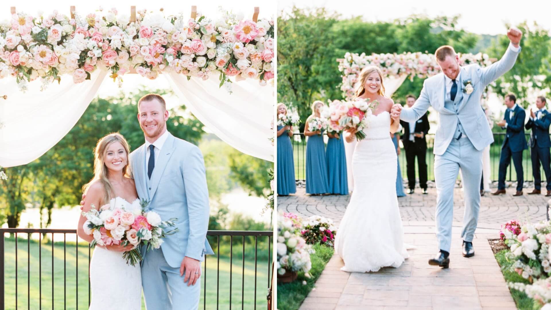 A couple poses under a floral arch and walks down the aisle celebrating at an outdoor wedding. The bride holds a bouquet, and the groom wears a light blue suit.