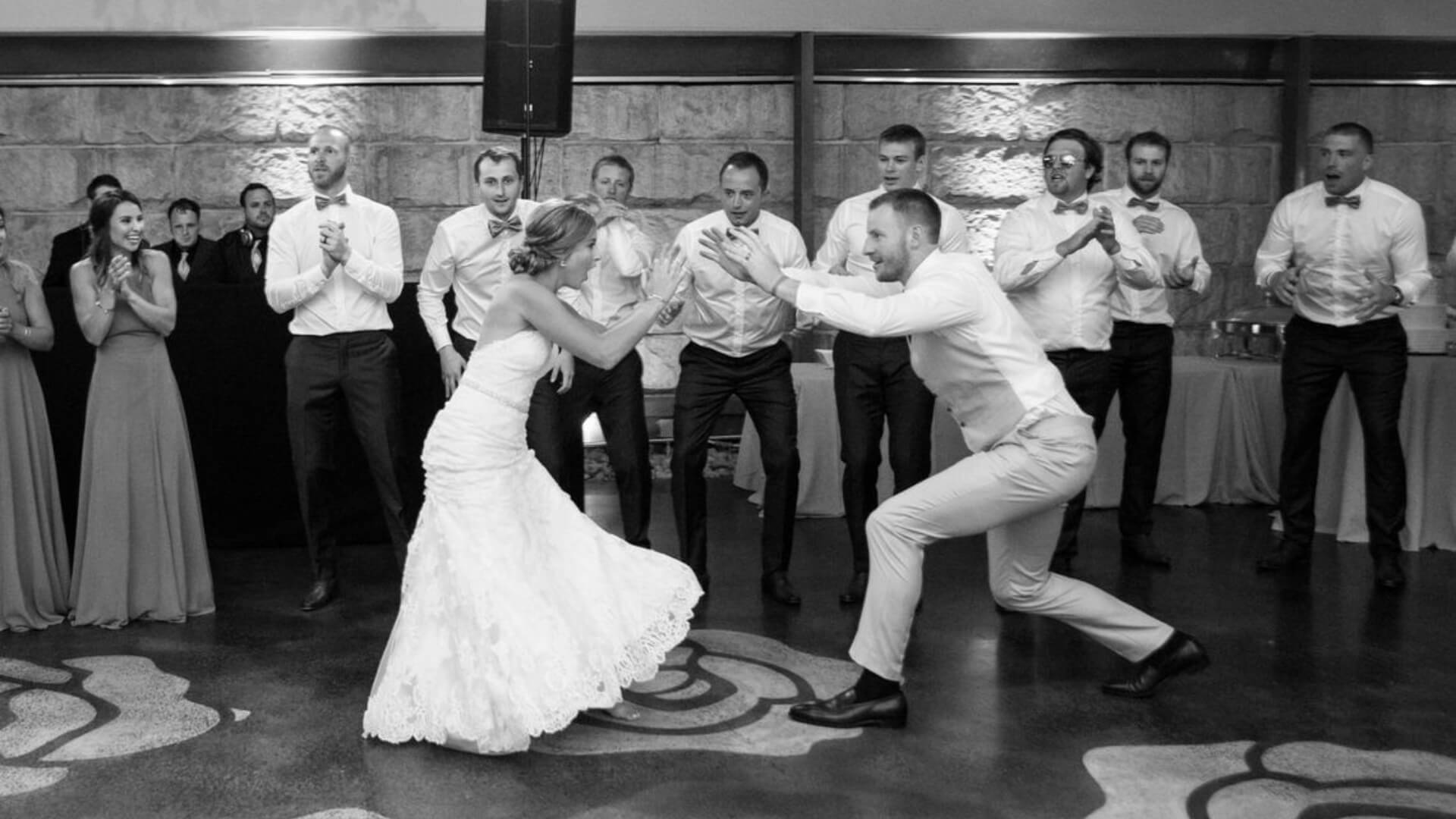 Bride and groom dance excitedly in front of cheering guests at a wedding reception.