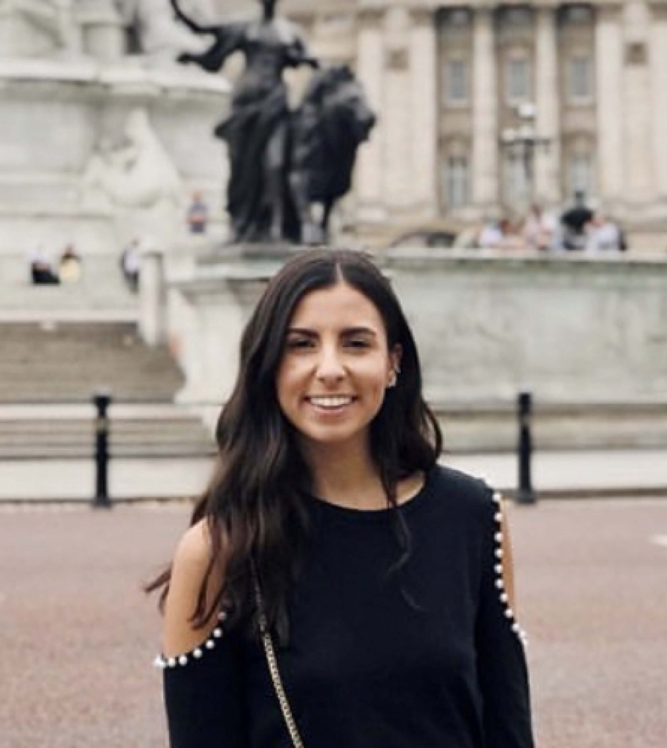 A woman with long dark hair and a black top stands outside in front of a large stone monument and statue.