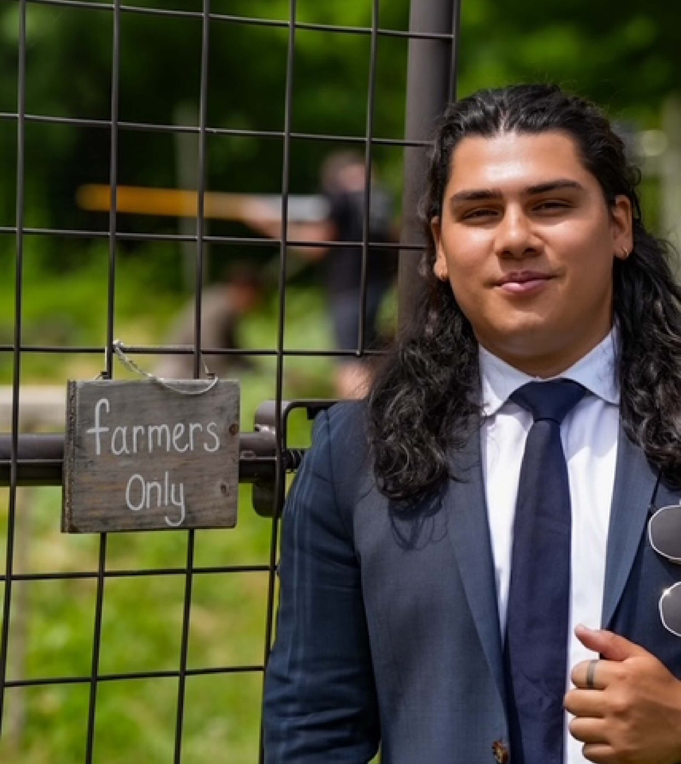 A person in a suit stands next to a metal gate with a sign that reads